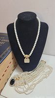 Overall lot, showing faux pearl necklaces displayed on bust with additional strands below