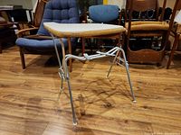 Side front view of the metal frame and desk base with wooden top rim held by silver tubular metal legs on a wooden floor