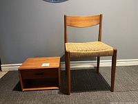 Photo showing the teak chair with corded seat alongside the teak floating nightstand on carpeted floor under neutral wall.