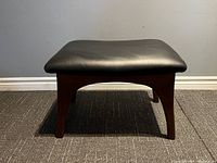 Front view of mid century style footstool ottoman showing teak legs and black leather seat
