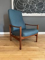 Front left three-quarter view of teak lounge chair with blue upholstery, showing frame and seat