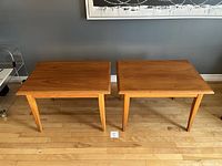 Pair of mid century modern teak end or side tables shown side by side on a hardwood floor against a gray wall.