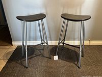 Pair of vintage IKEA bar stools with black seats and silver metal legs viewed angled from front.