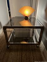 Vintage mid century modern chrome and brass coffee/side table with smoked glass shelves and casters shown from front and side angles with lamp on top.