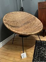 Front angle view of vintage woven wicker rattan hoop chair with black metal legs showing the overall condition and design.