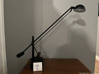 Side view showing entire black metal cantilever desk lamp on wooden surface with shadow on the wall.