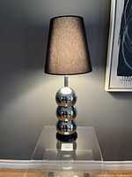Full view of the lamp turned on displaying the light through the black shade, showing the lamp height and reflective chrome balls.