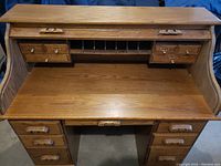 Front view of open secretary table showing multiple small drawers, cubby slots, and larger drawers underneath, with carved wooden handles.