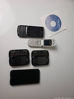 Top view of six cell phones arranged flat on a white surface, showing front screen/keyboards, accompanied by a BlackBerry Desktop Software CD