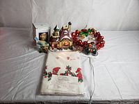 Overview of Christmas lot showing all items together including ceramic house, wreath, tablecloth, bird candle holder, and carriage figurine.