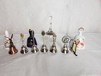 Eight decorative bells in assorted materials and designs on a white background