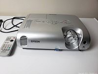 Front view of the silver Epson LCD projector with lens adjustment and remote control placed beside it.