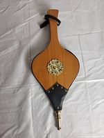 Wood and leather fireplace bellows lying flat, showing the full length and decorative brass medallion centerpiece