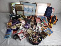 Overview of all items in the mixed lot showing toys, framed artwork, jewelry, craft supplies, and collectibles arranged on a white surface.