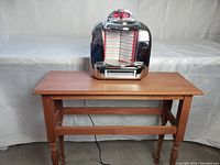 Wooden newspaper table with vintage radio placed on top, showing full view of table.