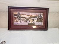 Frontal photo of the framed print showing a winter village scene with horse drawn sleigh, snowy streets, and buildings.