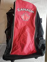 Photo showing red and black Canada rolling bag with maple leaf logo, front view.
