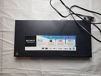 Top view of Sony Blu-ray DVD player with multimedia feature stickers and power cord.
