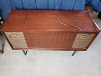 Front and side view of the wooden antique turntable and radio console showing wood paneling and woven cane speaker covers.