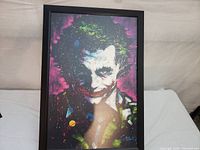Frontal view of the framed poster showing the vivid Joker artwork with colorful splashes and dark background.