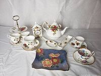 Full display of all vintage assorted tableware items including teapot, cups, saucers, plates, serving tray, and decorative clock.