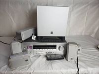 Full view of Yamaha HTR-5730 receiver with subwoofer on top and six small satellite speakers around. Remote control placed in front.