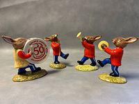 Four Royal Doulton Bunnykins porcelain figurines arranged showing front with instruments including bass drum, trumpet, cymbals, and drum major baton.