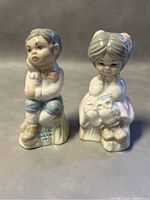 Front view of two porcelain figurines, a boy and a girl, showing detailed facial expressions and clothing. Both labeled Eaton's Collection Spain.
