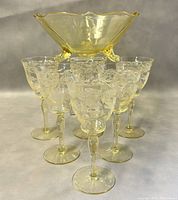 Photo showing six etched Mandarin Yellow aperitif goblets arranged in a semicircle around a footed serving bowl of the same glass and pattern.