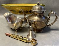 Image showing the full set of five items: silver plate footed gravy boat, ceramic serving bowl, silver-tone sugar or cream pot, decorative bell, and bullet replica bottle opener, arranged on a flat surface.