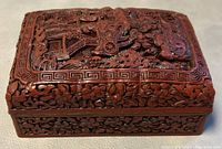 Top view of rectangular cinnabar lacquer box with carved relief scenes and floral border