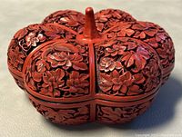 Front angled view showing detailed carving of flowers and birds on the gourd-shaped cinnabar lacquer trinket box.