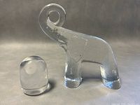Front view showing both clear glass elephant with curled trunk paperweight and smaller clear glass owl paperweight with rounded form and eye indentations.