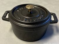 Mini round cast iron Staub cocotte in matte black with brass knob lid, photographed from above and side showing details