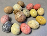 Collection of 15 polished marble eggs in multiple colors and patterns laid out on a gray surface.