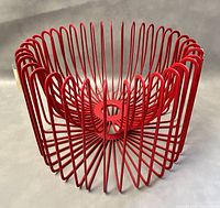 Front angled view of the red wire fruit bowl showing the geometric petal-like wire pattern and circular base.