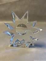 Front angle view of clear crystal sun paperweight showing sharp angular rays and central circular form.