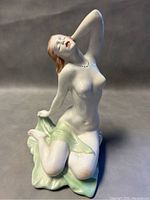 Front angle showing the nude woman figurine kneeling with hand behind head, displaying detailed facial features and delicate green cloth.