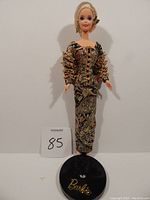 Front view of Barbie doll in ornate Christian Dior inspired evening gown on black Barbie stand