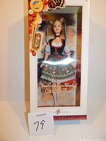 Barbie doll in original box, dressed in traditional Oktoberfest clothing featuring a green skirt with floral embroidery, white blouse, black corset, and ribbon hair accessories. Box is labeled 'Festivals of the World Oktoberfest'.