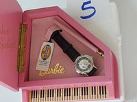 Barbie watch with black leather strap in pink box with piano key design and COA, showing Fossil brand tag.