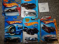 Photo showing five Hot Wheels Batmobile diecast cars in original packaging, arranged on carpet with a MaxSold lot tag number 70.