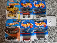 Six Hot Wheels die cast cars in original blister packaging arranged on carpeted surface. Each card shows the Hot Wheels logo and car details.