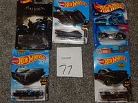 Five Hot Wheels die cast Batman and DC-inspired cars in new carded packaging, arranged on carpet with lot number 77 card visible.