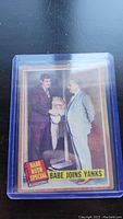 Photo of 1962 Topps Babe Ruth Special baseball card encased in clear plastic sleeve, showing image of two men in suits with text 'Babe Joins Yanks'.