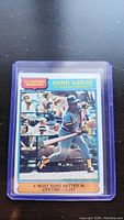 Photo of 1976 Topps Hank Aaron baseball card in protective sleeve, showing front artwork and text