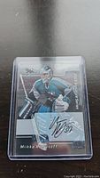2002-03 Pacific Snowy Scenes hockey card featuring goalie Mikka Kiprusoff in San Jose Sharks uniform with autograph and jersey patch. Card in protective plastic sleeve.