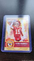 Photo shows 2017 rookie card of Patrick Mahomes II, Kansas City Chiefs, number 15, in a clear protective plastic case, with a fiery background design.
