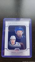 Quinn Hughes rookie hockey card in protective sleeve showing dual images of the player in Vancouver Canucks uniforms.