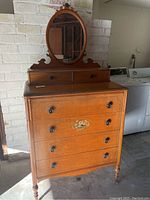 Full front view of antique wooden chest of drawers with attached oval mirror and decorative top section.